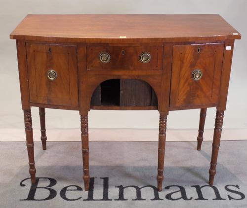 A Regency mahogany ebony strung bowfront sideboard, the centre drawer with a tambour door cupboard below, flanked by deep drawer and cellarette, on...