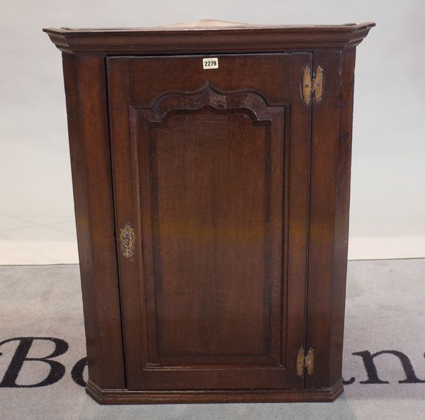 A George III oak wall hanging corner cabinet, enclosed by a mahogany crossbanded shaped raised and fielded panel door, 70cm wide x 93cm high.