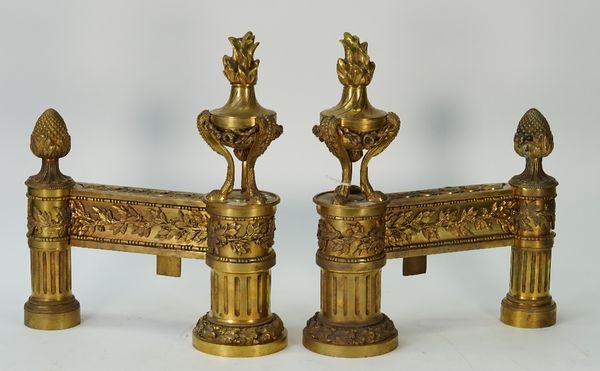 A pair of French ormolu chenets / andirons, Louis XVI style, late 19th century, with flaming urn finials and foliate cast supports, 39cm high, (2).