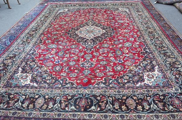 An Isfahan carpet, Persian, the madder field with a bold black and ivory medallion, matching spandrels, all with floral sprays; a complementary...