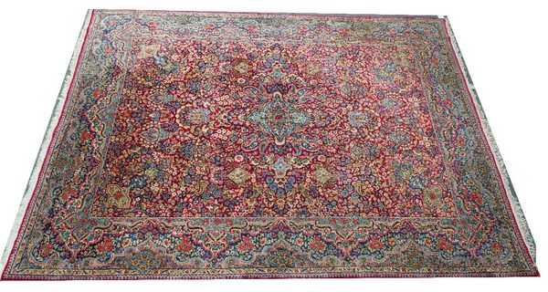 A Kerman carpet, Persian, the madder field with a central medallion, vase spandrels, all with abundantly floral sprays, an indigo border of waved...