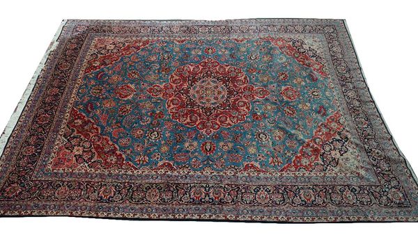 A Kashan carpet, Persian, the pale indigo field with a bold madder medallion, matching spandrels, delicate floral sprays, a dark indigo palmette...