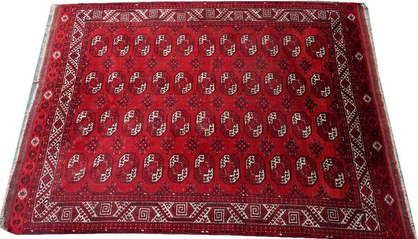 An Afghan carpet, the madder field with four columns of eleven single medallions, supporting cross motifs; an ivory barbed vine and diamond border,...