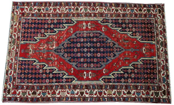 A Mazlaghan rug, Persian, the madder field with a serrated indigo medallion, matching spandrels; an ivory flower and waved vine border, 193cm x...