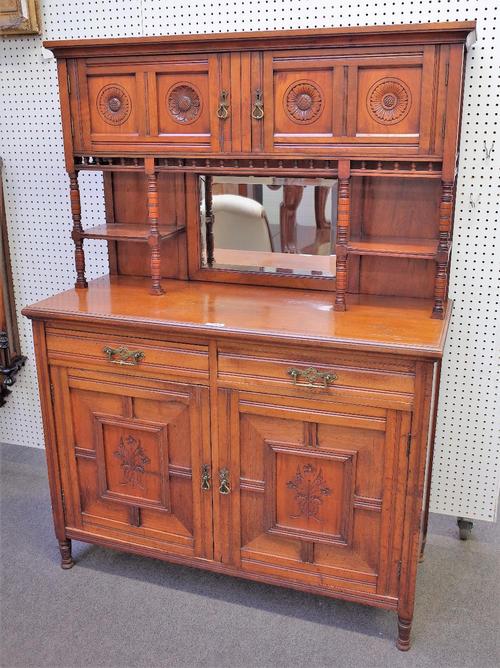An Aesthetic Movement walnut side cabinet, with four flower carved doors over bevelled mirror, the base with a pair of drawers over geometric moulded...