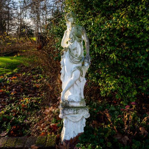 A RECONSTITUTED STONE FIGURE OF A SCANTILY CLAD FLOWER GIRL