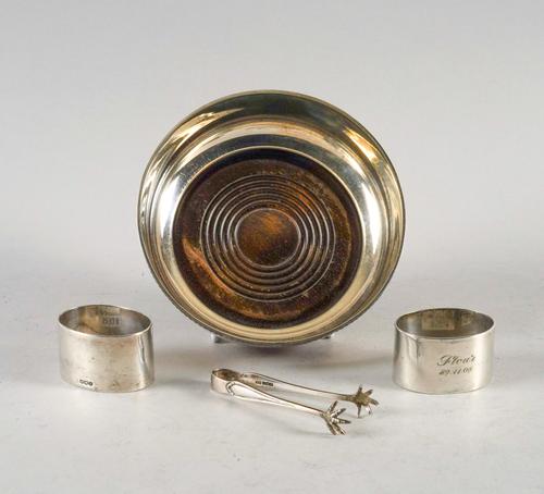 A SILVER MOUNTED BOTTLE COASTER, A PAIR OF SILVER NAPKIN RINGS AND A PAIR OF SUGAR TONGS (4)
