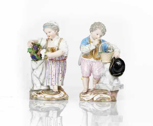 A pair of Meissen figures of children standing  beside columns, late 19th century,  the boy beside a basket of grapes, the girl with a bird inside...