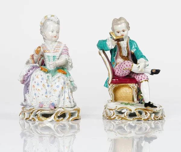 A pair of Meissen figures of children, late 19th century, modelled as a boy seated reading and a girl seated holding a shuttle, blue crossed swords...