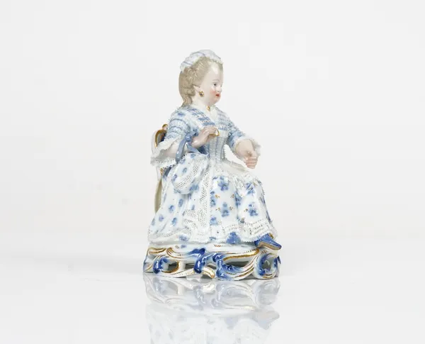 A Meissen figure of a girl, late 19th century, modelled seated holding a shuttle, painted predominantly in blue and gilt, blue crossed swords mark,...