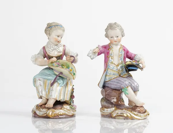 A pair of Meissen figures of a seated chidren, late 19th century,  modelled as a boy seated on a rocky mound with a hat full of flowers, and a girl...