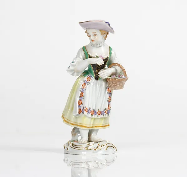 A Meissen figure of a girl, 20th century, modelled standing wearing a bonnet and dress, carrying a basket of flowers under her left arm and holding a...