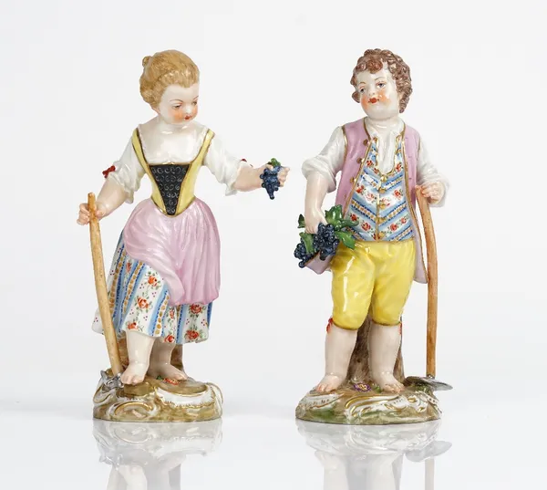 A pair of Meissen figures of child gardeners, 20th century, modelled as a boy and girl holding a hoe and bunch of grapes, blue crossed sword marks....
