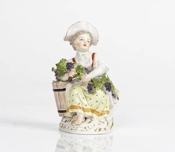 A Meissen figure of a girl vintner, 20th century, modelled seated beside a grape hod carrying a branch of grapes and a sickle, blue crossed swords...