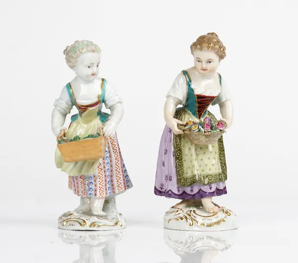 Two Meissen figures of girls, late 19th and 20th century, the first carrying a rectangular basket of flowers, the second with an oval basket basket...