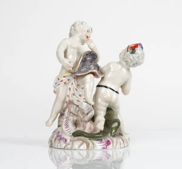 A German porcelain group of two putti, probably Meissen, emblematic of America and Europe, the former seated on the back of an alligator wearing a...