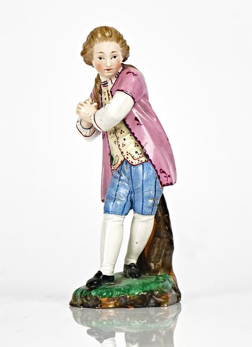 A Hochst Damn earthenware figure of a young man, 19th century, modelled standing before a tree stump with hands clasped, blue wheel mark and D,...