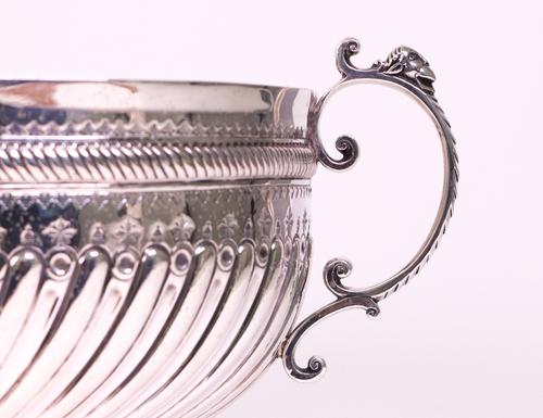 A late Victorian silver twin handled punch bowl, with spiral fluted decoration below a decorated band, the front with a rococo shaped cartouche, the...