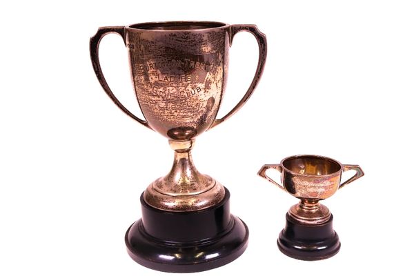 A silver twin handled trophy cup, presentation inscribed, height 14.5cm, Sheffield 1928, with a black stand and a silver twin handled small trophy...