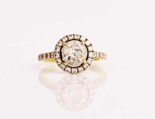 A gold and diamond ring, claw set with the principal circular cut diamond within a halo surround, set with smaller circular cut diamonds, between...