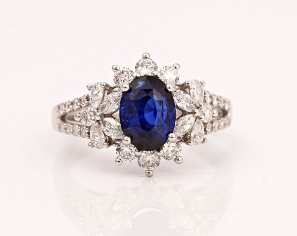 A platinum, sapphire and diamond cluster ring, claw set with the oval cut sapphire in a surround of circular and marquise cut diamonds between...