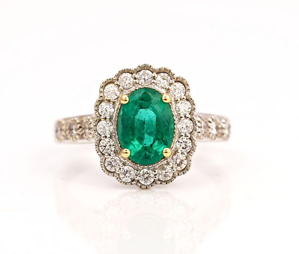 A white gold, emerald and diamond oval cluster ring, claw set with the oval cut emerald in a surround of circular cut diamonds, between diamond set...