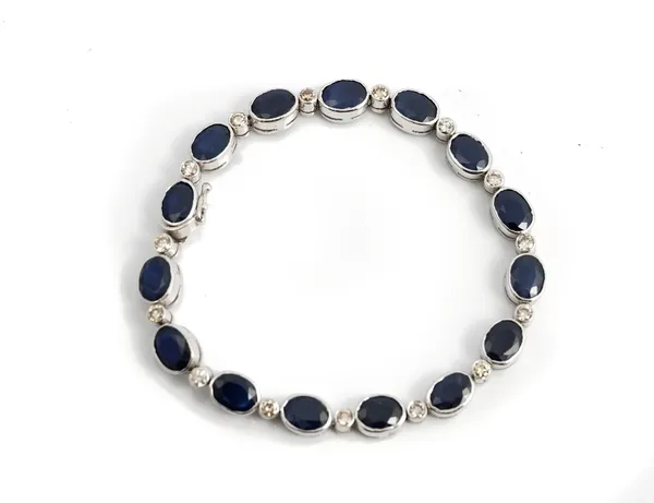 An 18ct white gold, sapphire and diamond bracelet, collet set with a row of oval cut sapphires alternating with collet set circular cut diamonds, on...