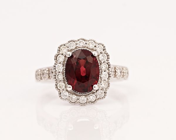 An 18ct white gold, red spinel and diamond cluster ring, claw set with the oval cut red spinel in a surround of circular cut diamonds, between...