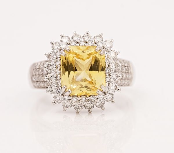 A platinum, yellow sapphire and diamond cluster ring, claw set with the octagon scissors cut yellow sapphire, in a two tier surround set with...