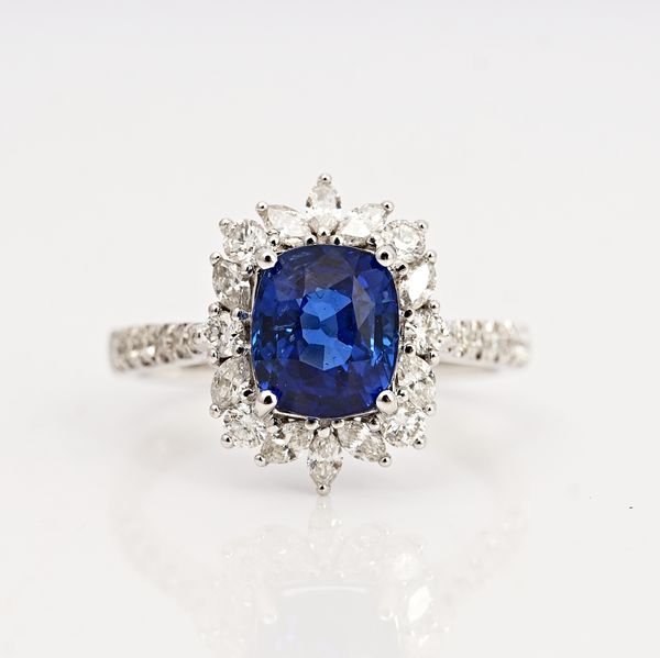 A white gold, sapphire and diamond cluster ring, claw set with the cushion shaped sapphire in a surround of marquise and circular cut diamonds,...
