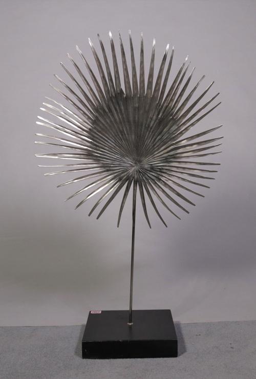 A modern slivered metal sun-burst sculpture on hardwood plinth base