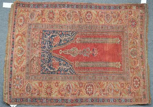 A Ghiordes prayer rug, Turkish, the madder mehrab with a hanging lantern, a pair of columns rising to an indigo arch of trailing branches with a...