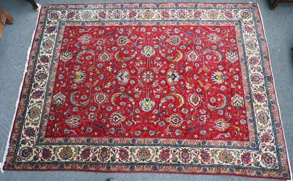 A Tabriz carpet, Persian, the madder field with a central diamond cross, supported by palmettes and floral sprays, an ivory palmette with leaf and...