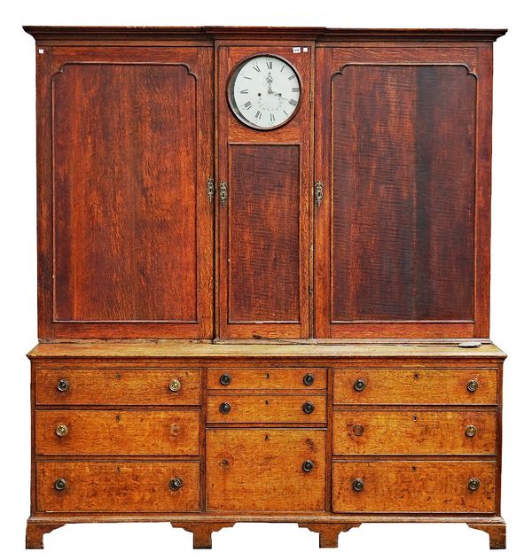 A George III oak housekeeper's cupboard with integral clock flanked by a pair of shaped panel doors over a nine drawer base on bracket feet, 209cm...