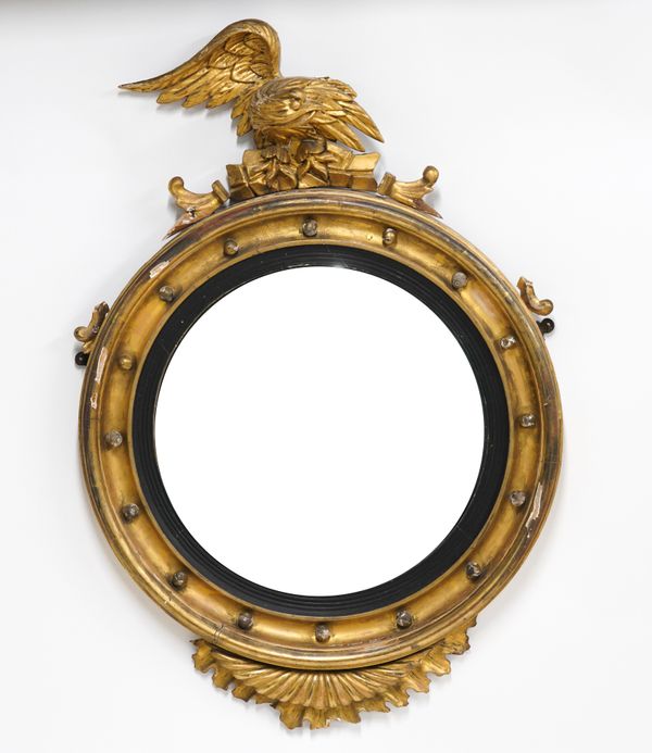 A REGENCY GILT FRAMED CONVEX WALL MIRROR WITH EAGLE SURMOUNT AND EBONISED SLIP