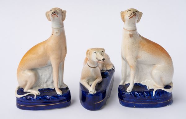 A STAFFORDSHIRE POTTERY RECUMBENT GREYHOUND PEN HOLDER AND A PAIR OF SEATED GREYHOUNDS (3)