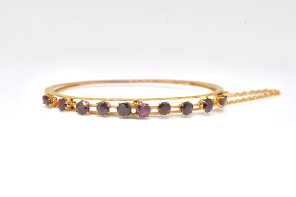 A GOLD AND GARNET OVAL HINGED BANGLE