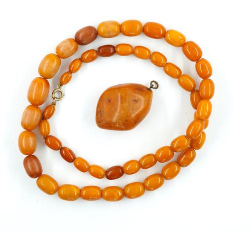 A SINGLE ROW NECKLACE OF VARICOLOURED BUTTERSCOTCH COLOURED GRADUATED OVAL AMBER BEADS AND A DROP SHAPED PENDANT (2)