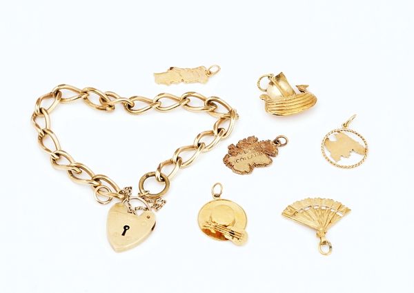 A gilt metal curb link bracelet, fitted with a 9ct gold heart shaped padlock clasp and six gold charms (7)