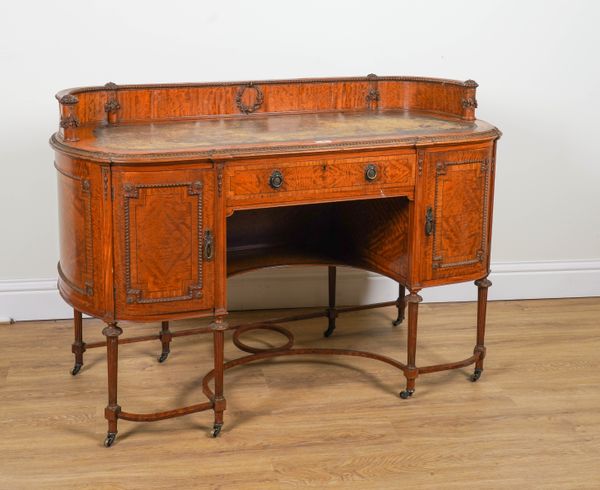 PROBABLY WARING & GILLOWS; AN EARLY 20TH CENTURY CARVED SATINWOOD ROUNDED RECTANGULAR WRITING DESK ON TAPERING FLUTED SUPPORTS