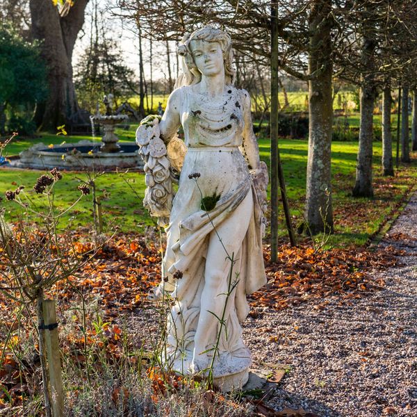 A RECONSTITUTED STONE FIGURE OF A SCANTILY CLAD FLOWER MAIDEN