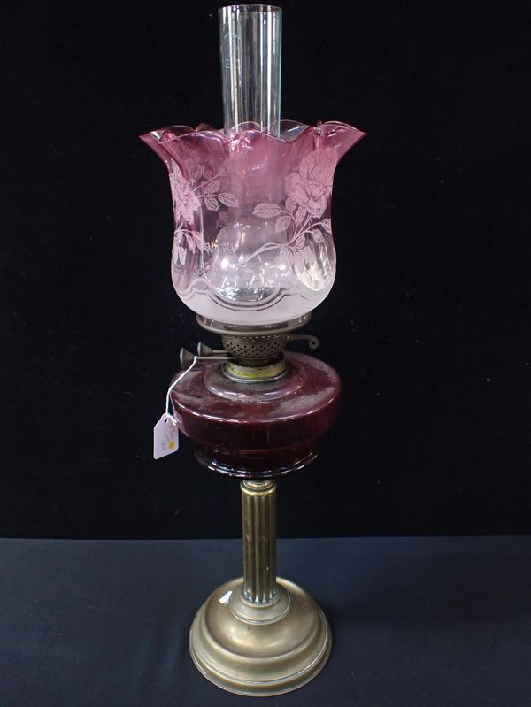 A CRANBERRY GLASS OIL LAMP ON BRASS STAND