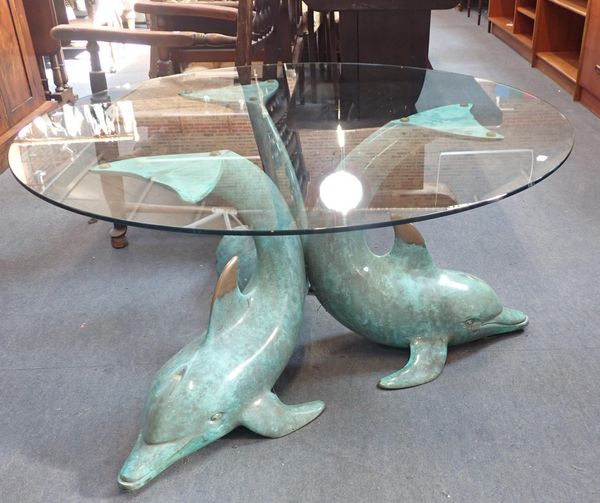 A GLASS TOPPED COFFEE TABLE ON BRONZED TRIPLE DOLPHIN STAND