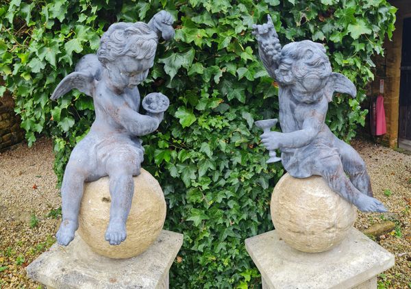 A PAIR OF CAST LEAD CHERUBS UPON COMPOSITION STONE SPHERES