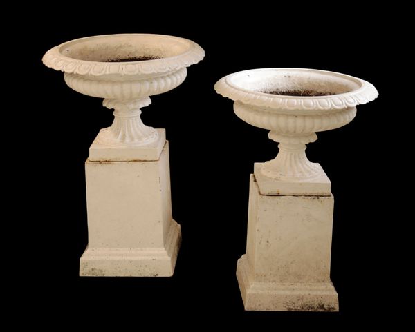 A PAIR OF VICTORIAN WHITE PAINTED CAST IRON GARDEN URNS ON PLINTHS,