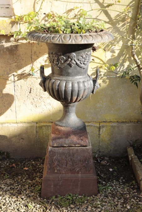 A PAIR OF CAST IRON TWIN HANDLED GARDEN URNS ON PLINTHS,