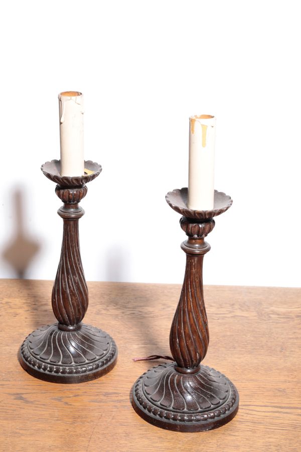 A PAIR OF ITALIAN CARVED AND STAINED WALNUT CANDLESTICKS FITTED AS TABLE LAMPS,