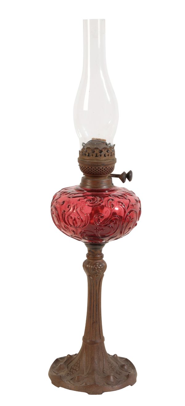 AN ART NOVEAU CAST IRON AND CRANBERRY GLASS OIL LAMP