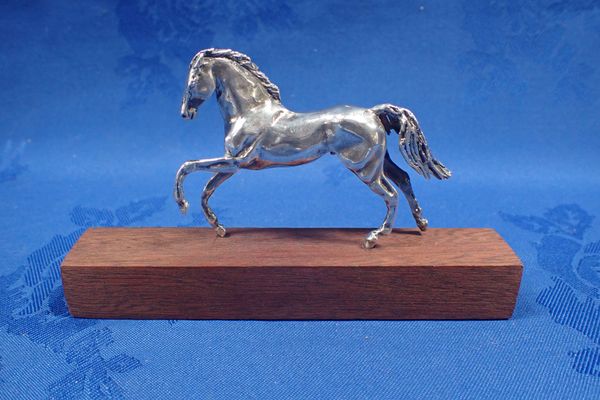 A SILVER HORSE MOUNTED ON A WOODEN BLOCK