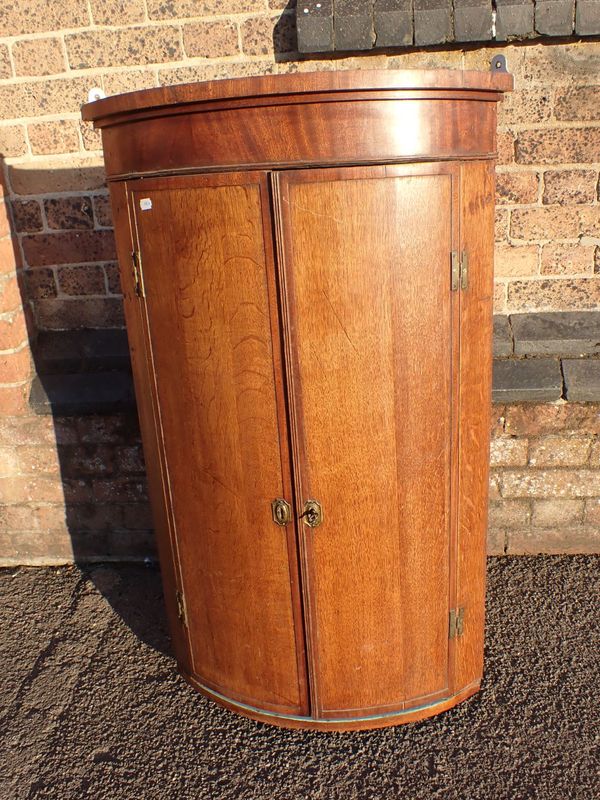 A 19TH CENTURY BOWFRONT OAK HANGING CORNER CUPBOARD